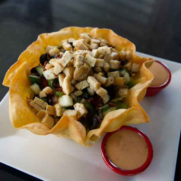 A taco salad in a crispy tortilla bowl with chicken, vegetables, and two sides of dressing.