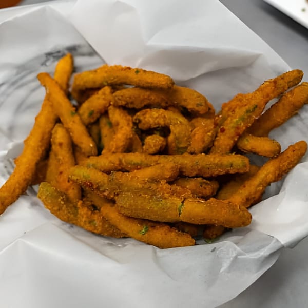 A basket of golden-brown fried pickle spears, a popular sports bar appetizer, served in white paper.