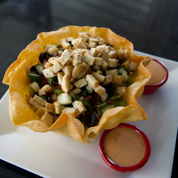 A taco salad in a crispy tortilla bowl with chicken, vegetables, and two sides of dressing.