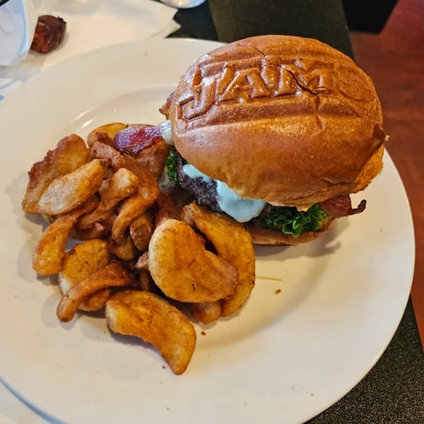 A Jams@209 burger with a branded bun, bacon, lettuce, and sauce, served with crispy fries.