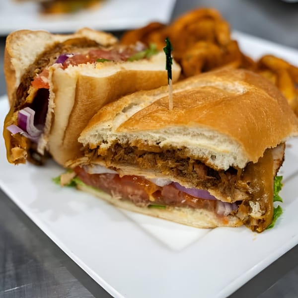 A Jams@209 Sports Bar & Grill sandwich, cut in half, with meat, lettuce, tomato, and onion.