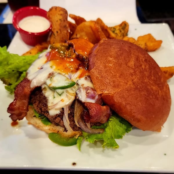 A Jams@209 Sports Bar & Grill burger with bacon, cheese, jalapenos, onions, and a side of potato wedges.