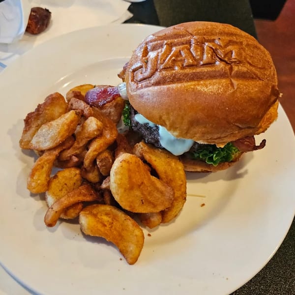 A Jams@209 burger with a branded bun, bacon, and sauce, served with crispy wedge fries.