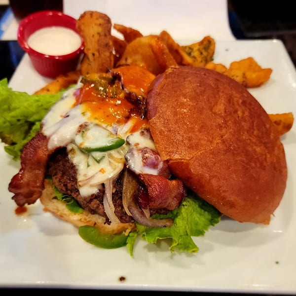 A Jams@209 Sports Bar & Grill burger with melted cheese, bacon, jalapeños, and a side of potato wedges.