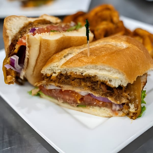 A Jams@209 Sports Bar & Grill pulled pork sandwich with lettuce, tomato, and onion on a white plate.