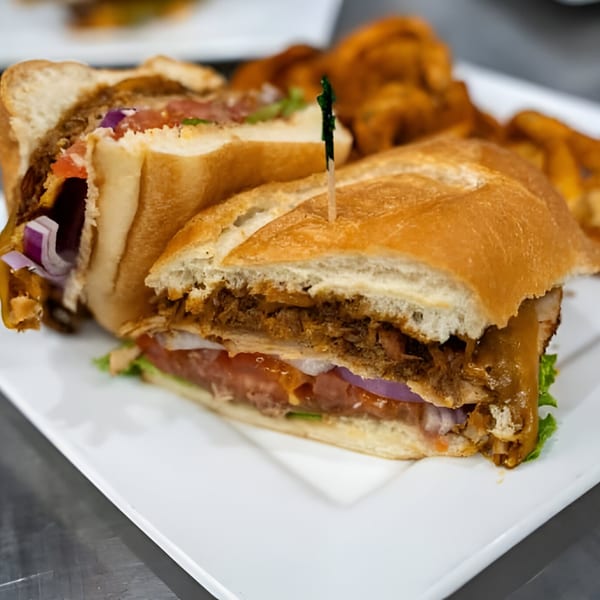 Pulled pork sandwich with lettuce, tomato, and red onion, served with sweet potato fries.