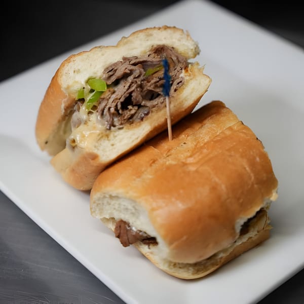A sliced Philly cheesesteak sandwich with melted cheese and green peppers on a white plate.
