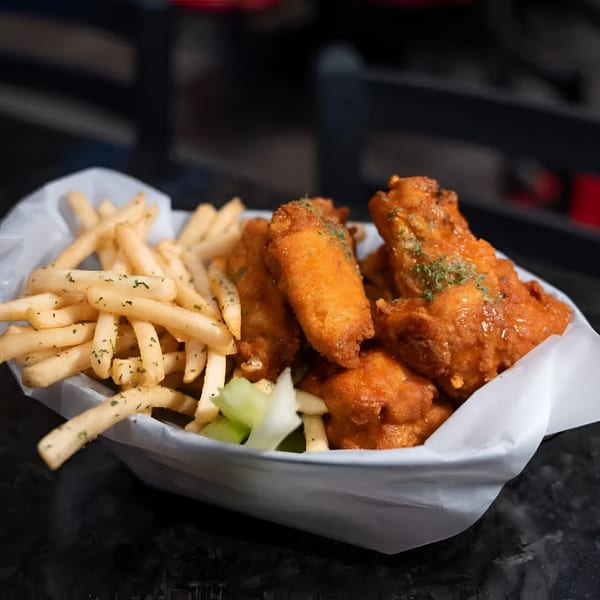 Crispy golden-brown chicken wings and french fries with herbs, served in a white paper-lined basket.