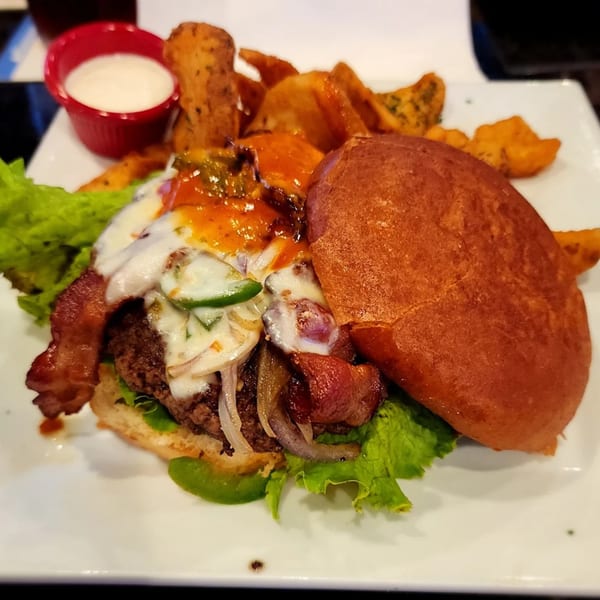 A Jams@209 Sports Bar & Grill burger with bacon, cheese, jalapenos, and fries on a white plate.
