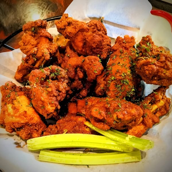 A basket of Jams@209's crispy, saucy chicken wings, garnished with herbs and served with celery sticks.