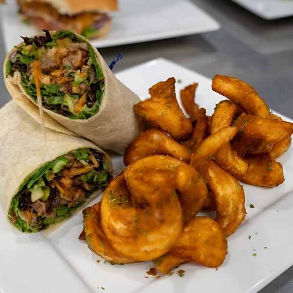 A Jams@209 Sports Bar & Grill wrap filled with meat and greens, served with seasoned potato wedges.