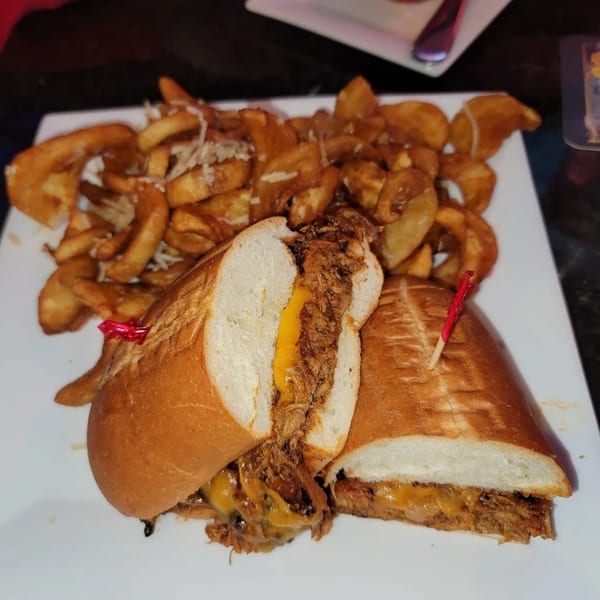 A pulled pork sandwich with melted cheese and a side of seasoned wedge fries on a white plate.