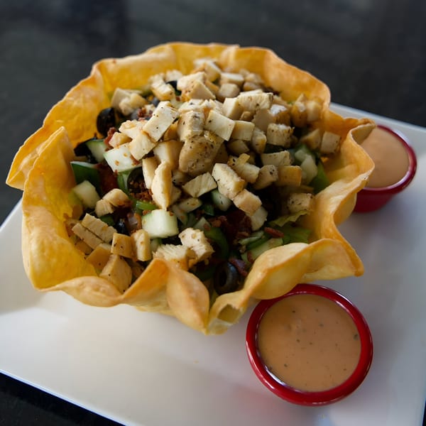 A Jams@209 Sports Bar & Grill taco salad in a crispy shell with two sides of dressing.