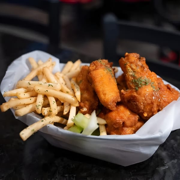 A basket of crispy golden fries and saucy orange chicken wings with celery sticks.