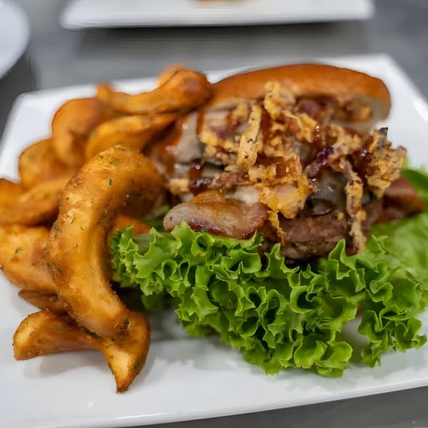 A Jams@209 Sports Bar & Grill sandwich with crispy onions, meat, and lettuce, served with curly fries.