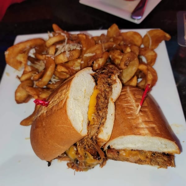 Pulled pork sandwich with melted cheese and a side of seasoned wedge fries on a white plate.